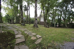 Stroll through the lush landscape along the winding stone pathway, surrounded by mature trees and a serene atmosphere.