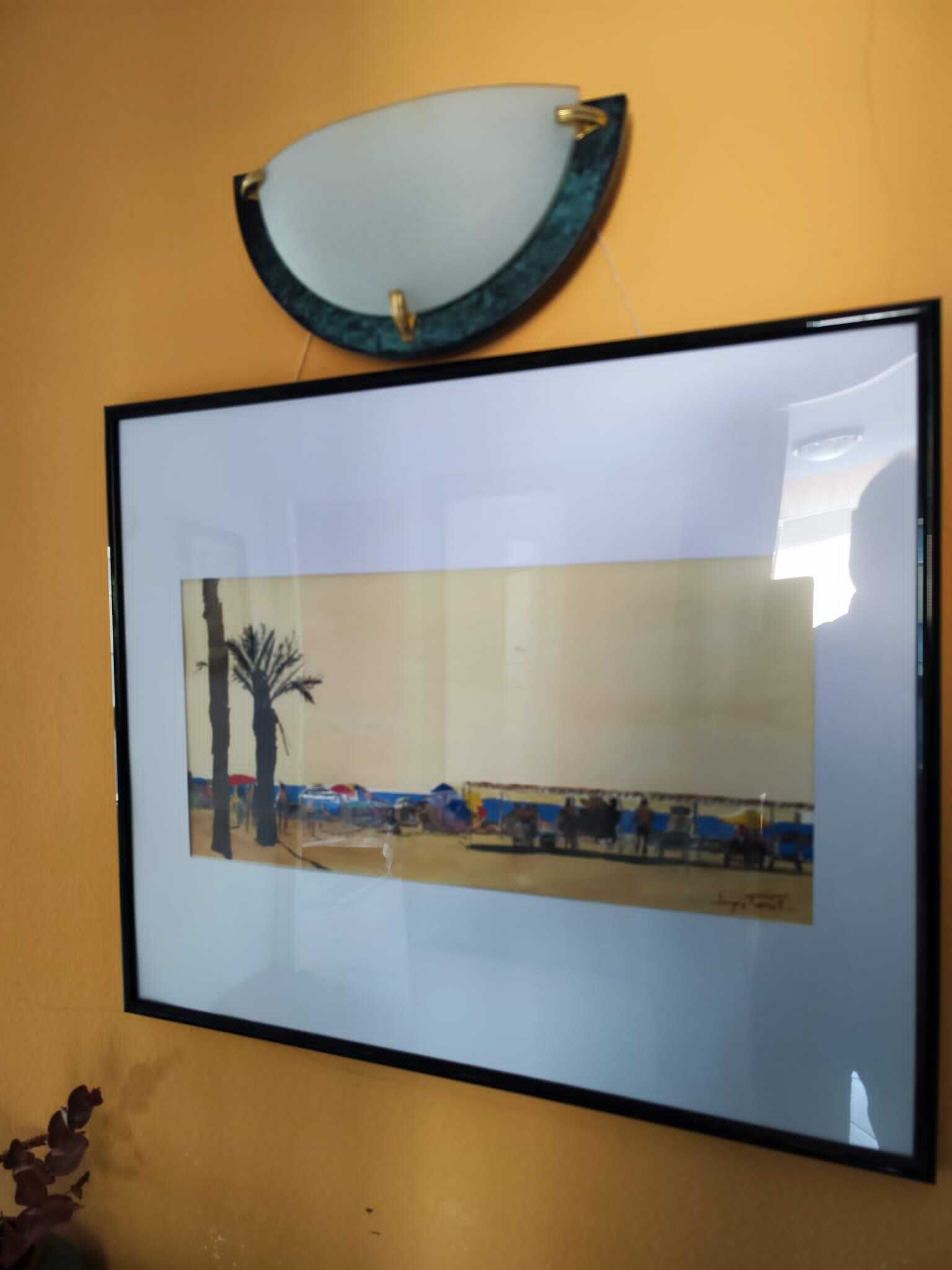 Obra emoldurada retratando uma cena de praia com palmeiras e pessoas.