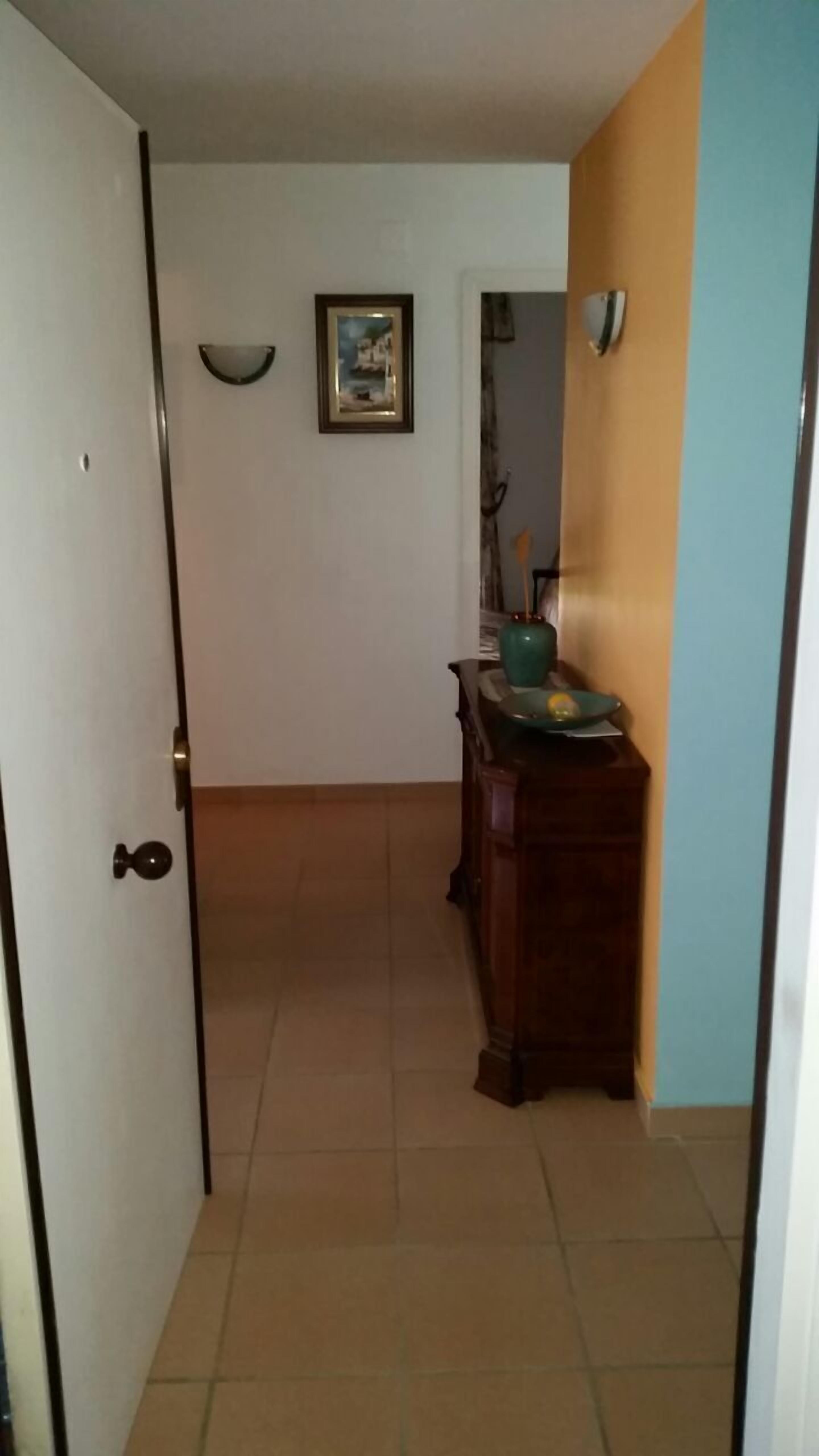 A hallway with a closed door, a framed picture on the wall, and a wooden cabinet with a vase and a plate.