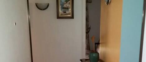 A hallway with a closed door, a framed picture on the wall, and a wooden cabinet with a vase and a plate.