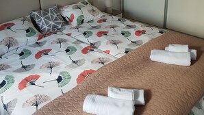 A neatly made bed with a patterned bedspread, a quilted brown blanket, and folded towels.