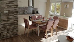 A modern kitchen with a dining area, wooden cabinets, a microwave, and a window with a view of trees.