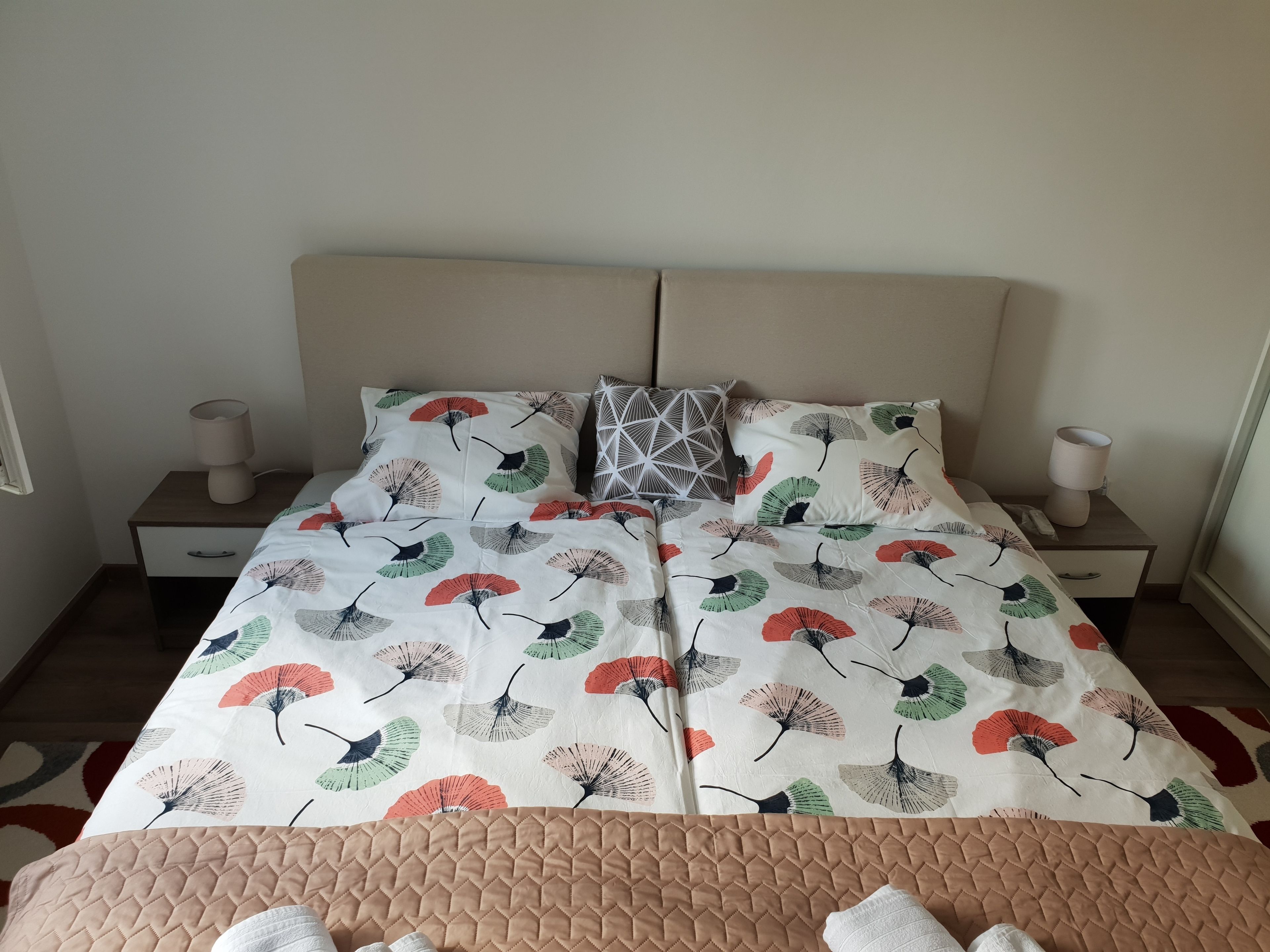 Una cama doble con cubrecama floral, dos mesitas de noche con lámparas y una manta acolchada.