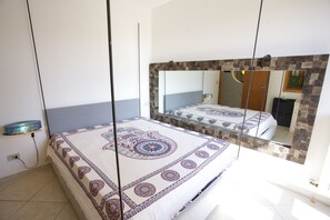 Una camera da letto con un grande specchio, un letto con copriletto decorato, un comodino e una mensola a parete.