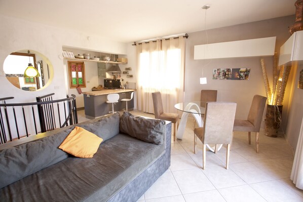 Un soggiorno moderno con un divano grigio, un'area pranzo con tavolo e sedie, e una cucina sullo sfondo.