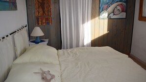A bedroom with a large bed, a nightstand with a lamp, and two paintings on the wall. - Stylishly designed apartment with magnificent sea views in a stunning natural environment (Portixeddu)