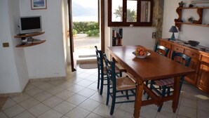 A dining area with a wooden table, chairs, and a television on a shelf. - Stylishly designed apartment with magnificent sea views in a stunning natural environment (Portixeddu)