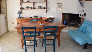 A dining area with a wooden table and chairs, a blue sofa, and a fireplace. - Stylishly designed apartment with magnificent sea views in a stunning natural environment (Portixeddu)