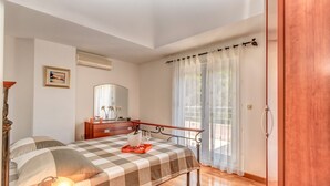 Ein Schlafzimmer mit kariertem Bettbezug, einer Nachttischlampe, einem Schminktisch, einem Spiegel und einem Fenster mit durchsichtigen Vorhängen.
