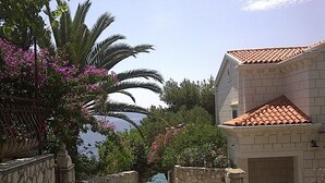 Ein gepflasterter Weg führt zu einem Gebäude mit einem Ziegeldach, umgeben von üppigem Grün und Blick aufs Meer.