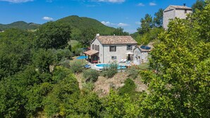 A stone house with a pool and outdoor seating, surrounded by lush greenery and hills.