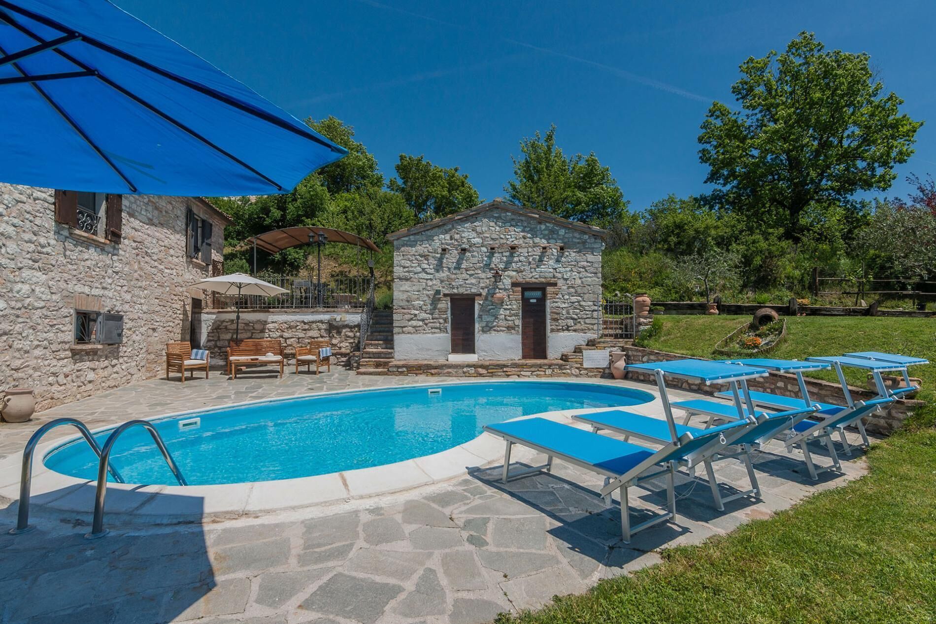 A stone building with a pool, outdoor seating, and umbrellas.