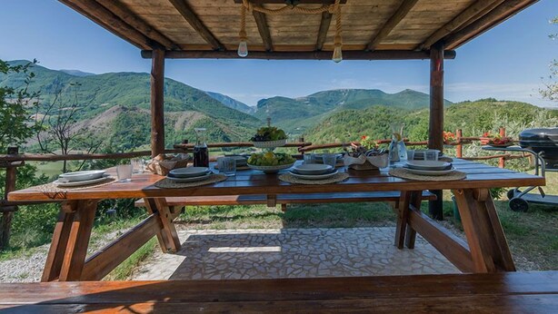 A wooden table set outdoors with a view of green hills.
