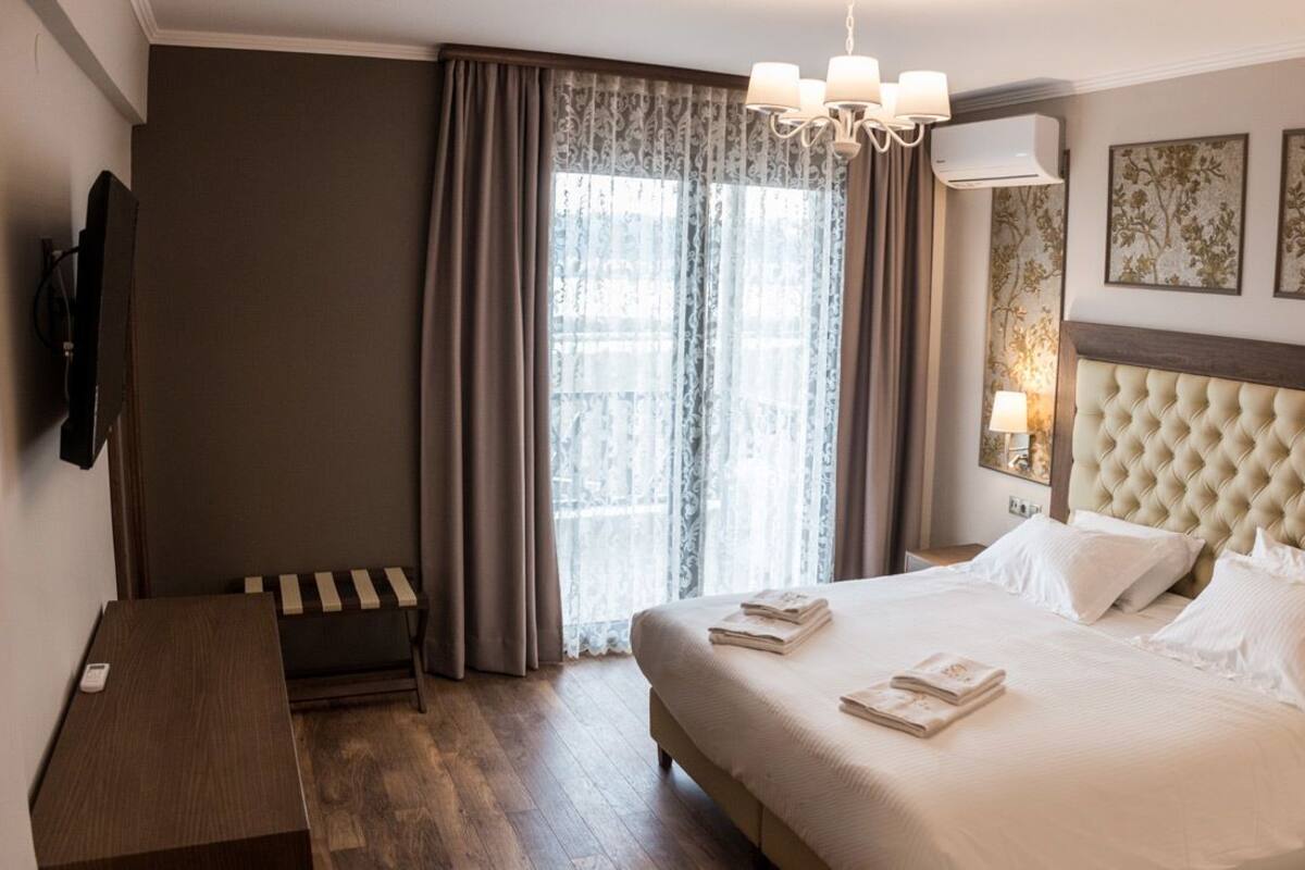 Ein Hotelzimmer mit einem großen Bett, einem Nachttisch, einem Fernseher und einem Fenster mit Vorhängen.