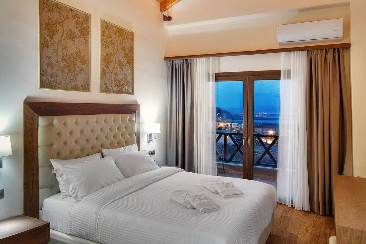 Ein Schlafzimmer mit einem großen Bett, Holzbalkendecke, einem Balkon mit Vorhängen und Blick auf die Stadt.