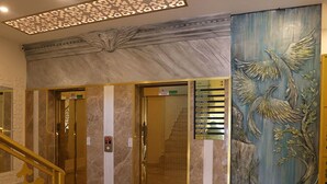 Un vestíbulo con suelo de mármol, una escalera y un mural grande con un pájaro.