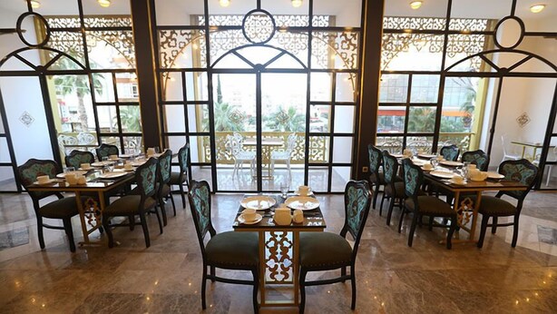 Un restaurante con varias mesas y sillas, amplias ventanas con celosías decorativas y vistas al exterior.