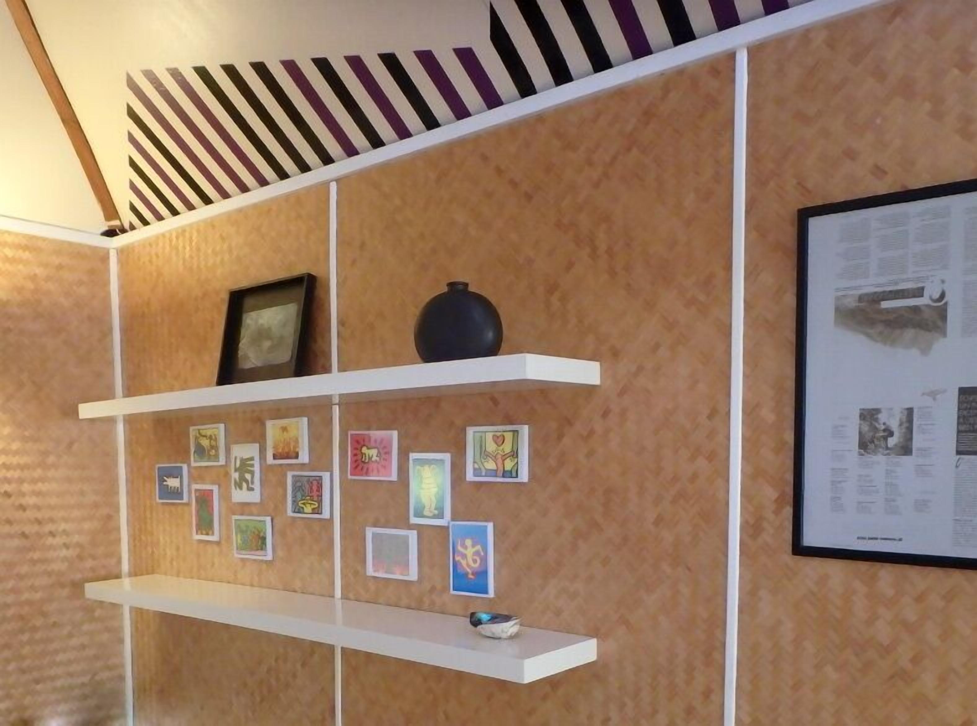 Una stanza con pareti rivestite in legno, mensole bianche che espongono opere d'arte incorniciate e un giornale incorniciato a destra.