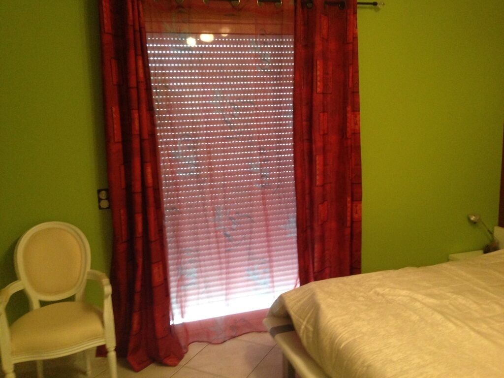 Une chambre à coucher avec un lit, une chaise et une fenêtre ornée de rideaux rouges.