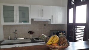 Une cuisine avec des armoires blanches, un évier en acier inoxydable et un four à micro-ondes. Un saladier rempli de fruits est posé sur le comptoir.