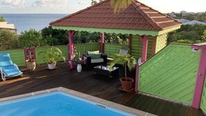 Un espace piscine agrémenté d’un kiosque, de chaises longues et de plantes en pot.