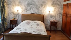 Une chambre à coucher comprenant un lit, deux tables de chevet, une armoire et un mur décoré d’une fresque représentant un arbre.