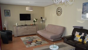 Un salon avec un canapé, une table basse, un téléviseur, une horloge et une lampe.