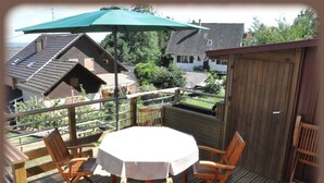 Une terrasse en bois avec une table ronde et quatre chaises, un parasol vert et une clôture en bois.