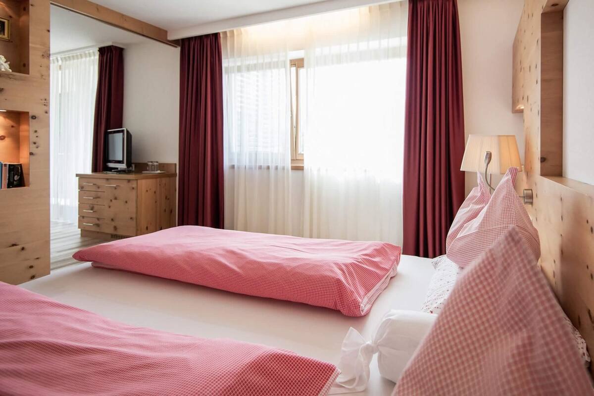 A hotel room with two beds, a wooden dresser, a television, and a window with curtains.