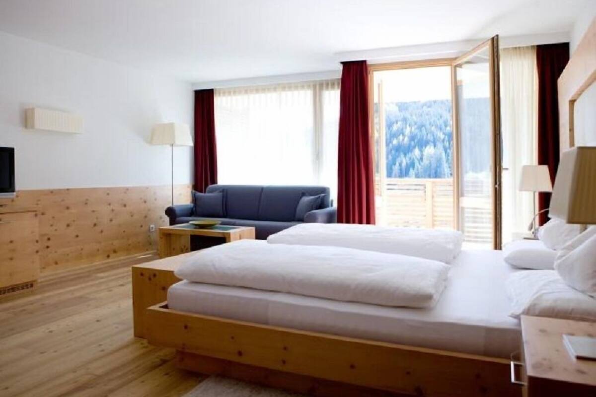 A bedroom with a wooden bed, a blue sofa, and a view of a snowy landscape through the window.