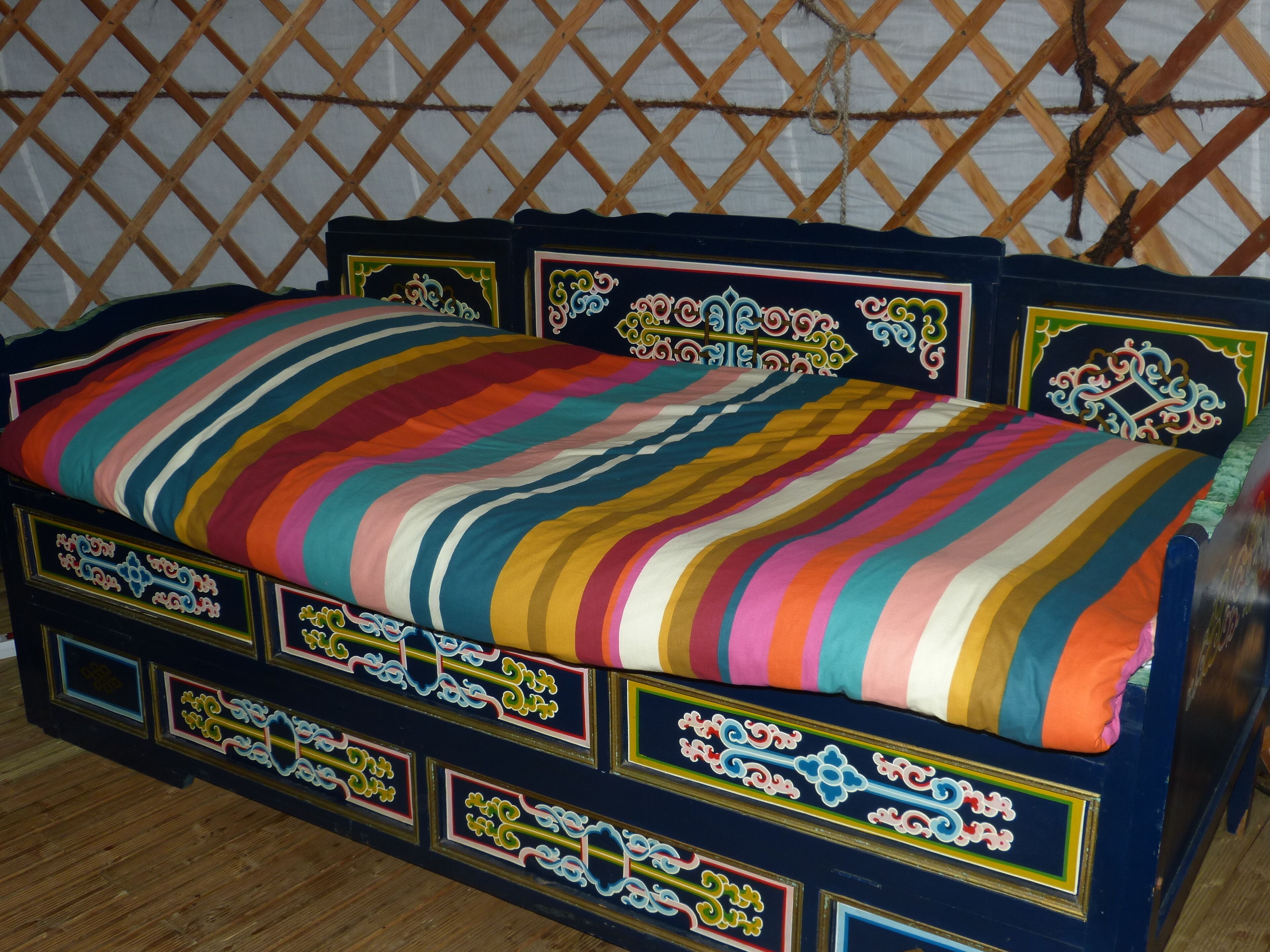 A bed with a colorful striped blanket and ornate headboard with decorative panels.