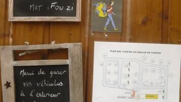 Eine Holzwand mit drei Elementen: einer Tafel mit einer Willkommensbotschaft, einem Buch mit dem Titel 'RECOMMANDÉ PAR le routard 2012' und einer Karte mit der Aufschrift 'PLAN DES YOURTES DU VILLAGE DE YOURTES'.