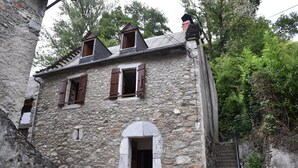 Edifici de pedra amb una porta central d'arc, persianes de fusta i una petita finestra al menjador.