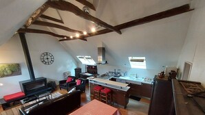 Un espai vital compacte amb una cuineta, una zona de menjador amb mantell vermell a quadres, un sofà i una televisió.
