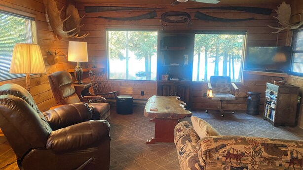 A cozy cabin interior with wooden walls, a leather recliner, a patterned sofa, a wooden coffee table, and a television.