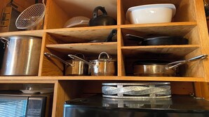 A kitchen with wooden shelves holding various kitchenware, including pots, pans, and a kettle.