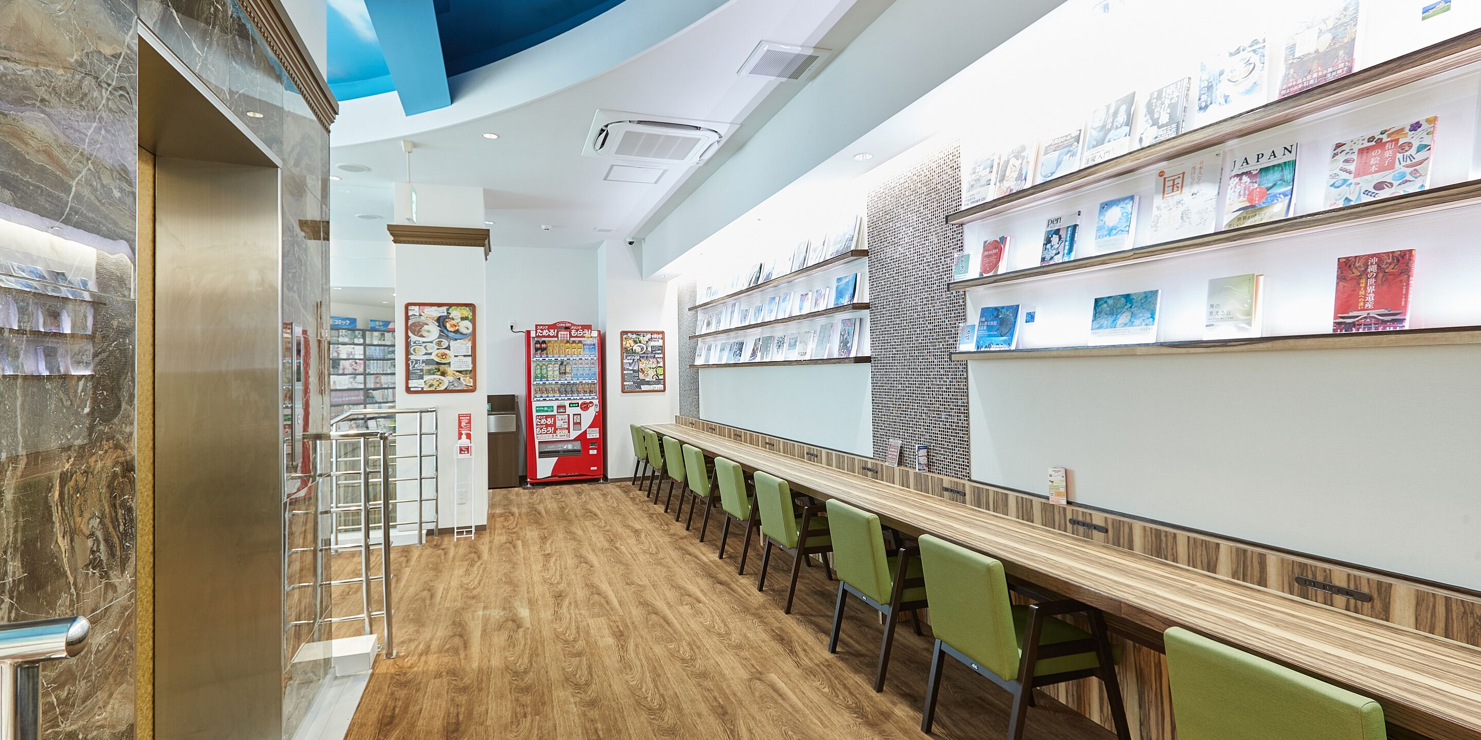 A modern interior with a long wooden table, green chairs, and a wall with bookshelves.