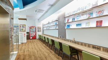 A modern interior with a long wooden table, green chairs, and a wall with bookshelves.