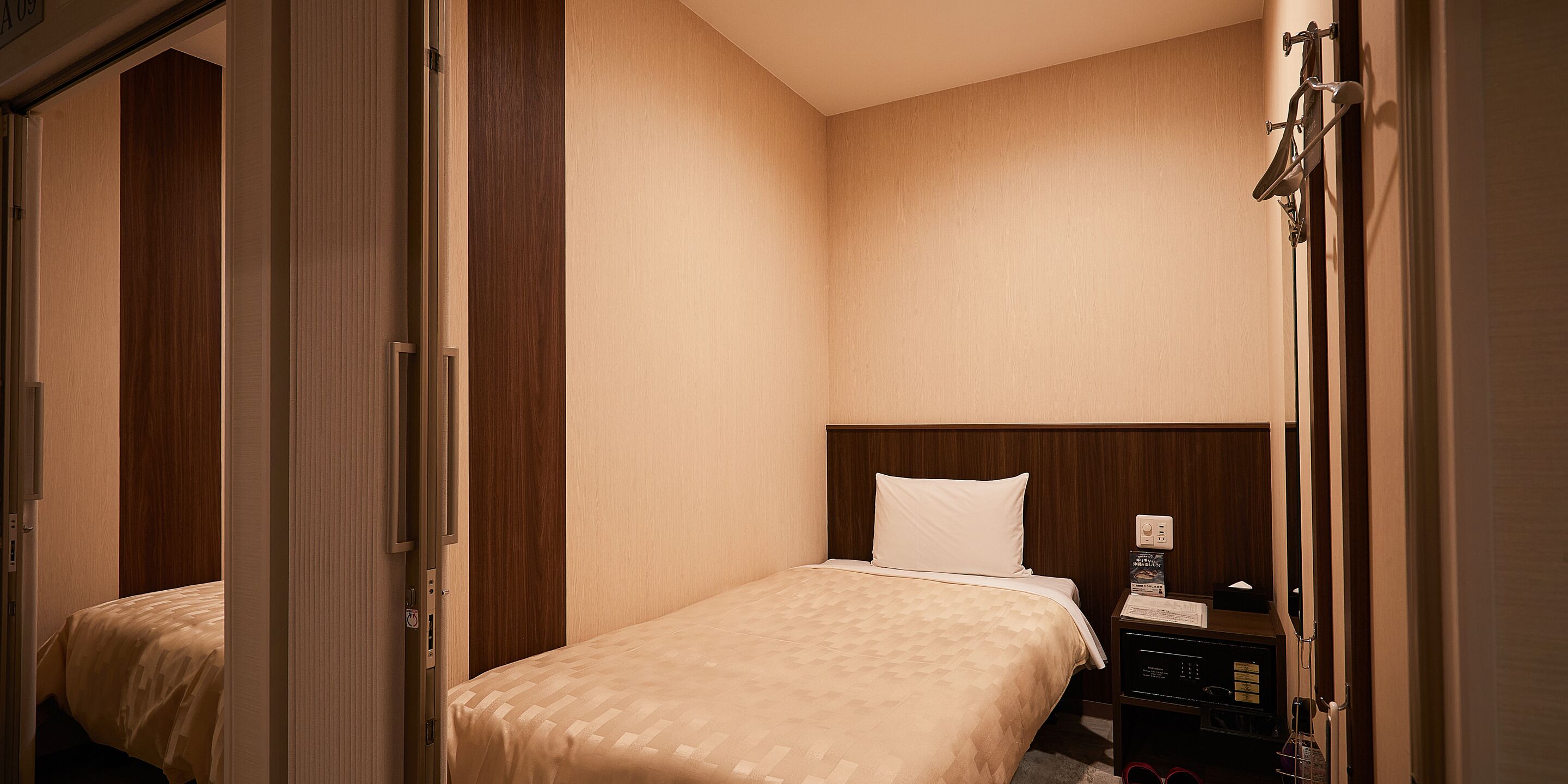 A hotel room with a bed, a wooden headboard, a nightstand, and a door leading to another room.