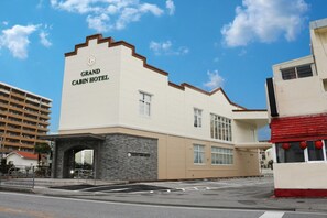 The exterior of the Grand Cabin Hotel with a prominent entrance, a stone archway, and a clear blue sky. - Grand Cabin Hotel Naha Oroku (Naha)