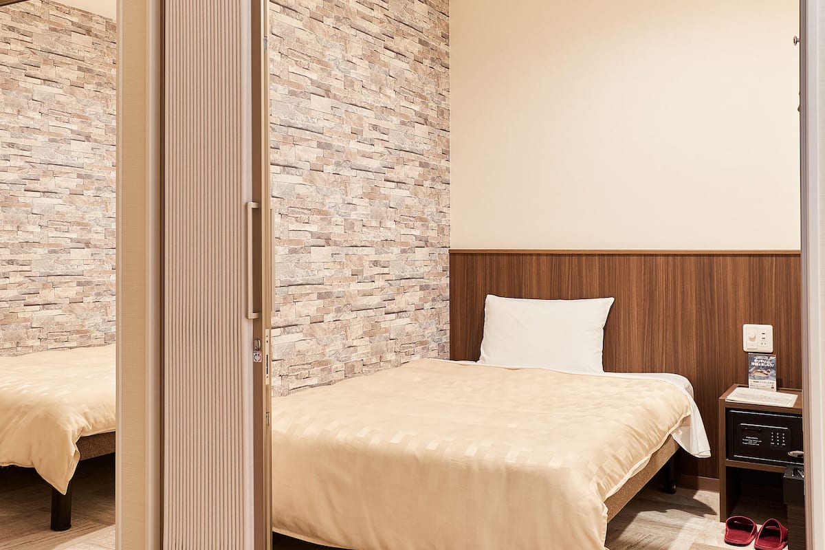 A hotel room with two beds, a wooden headboard, a nightstand with a radio, and a stone-patterned wall.