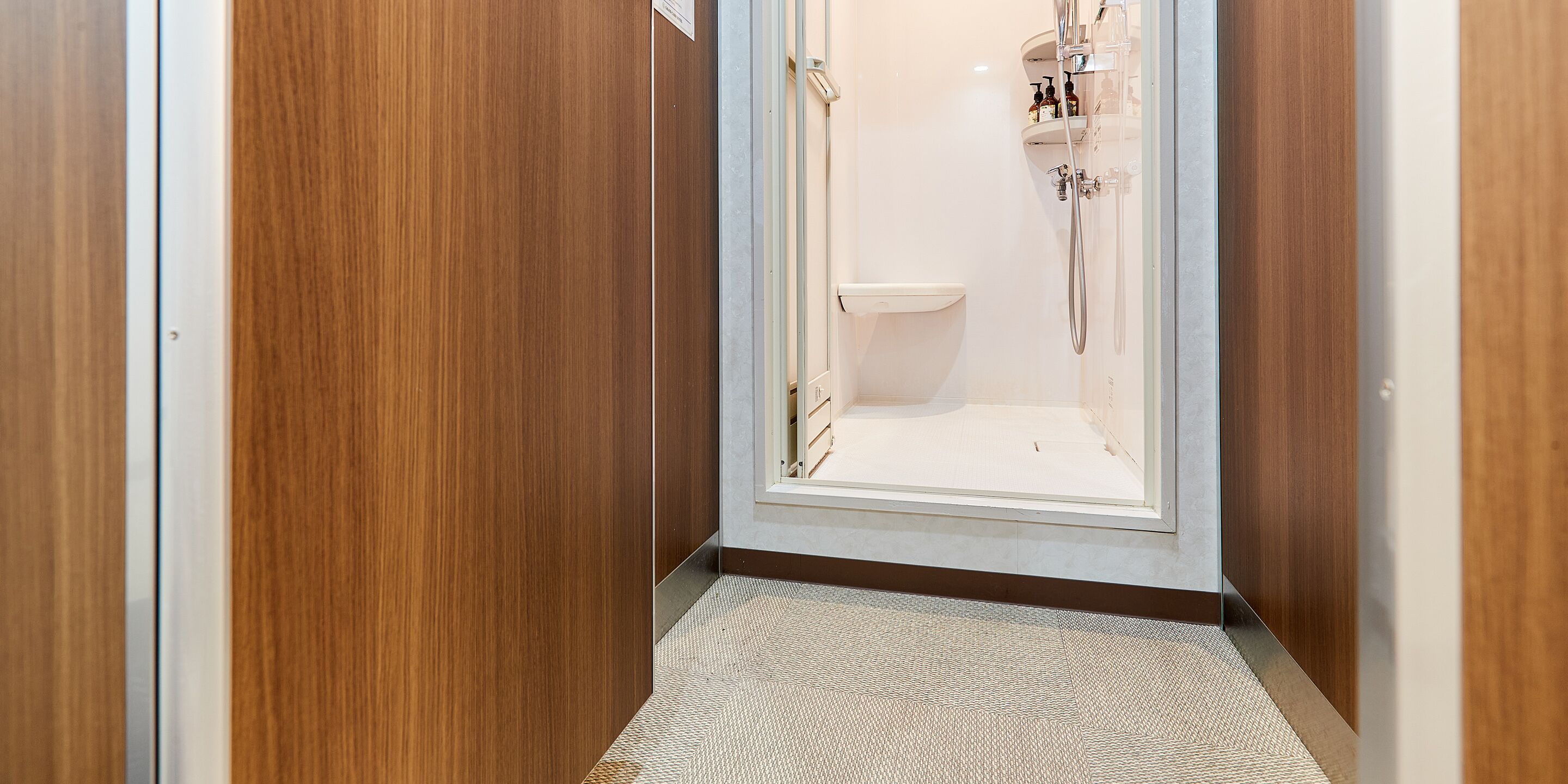 Een smalle gang die leidt naar een doucheruimte met een toilet en een wastafel.