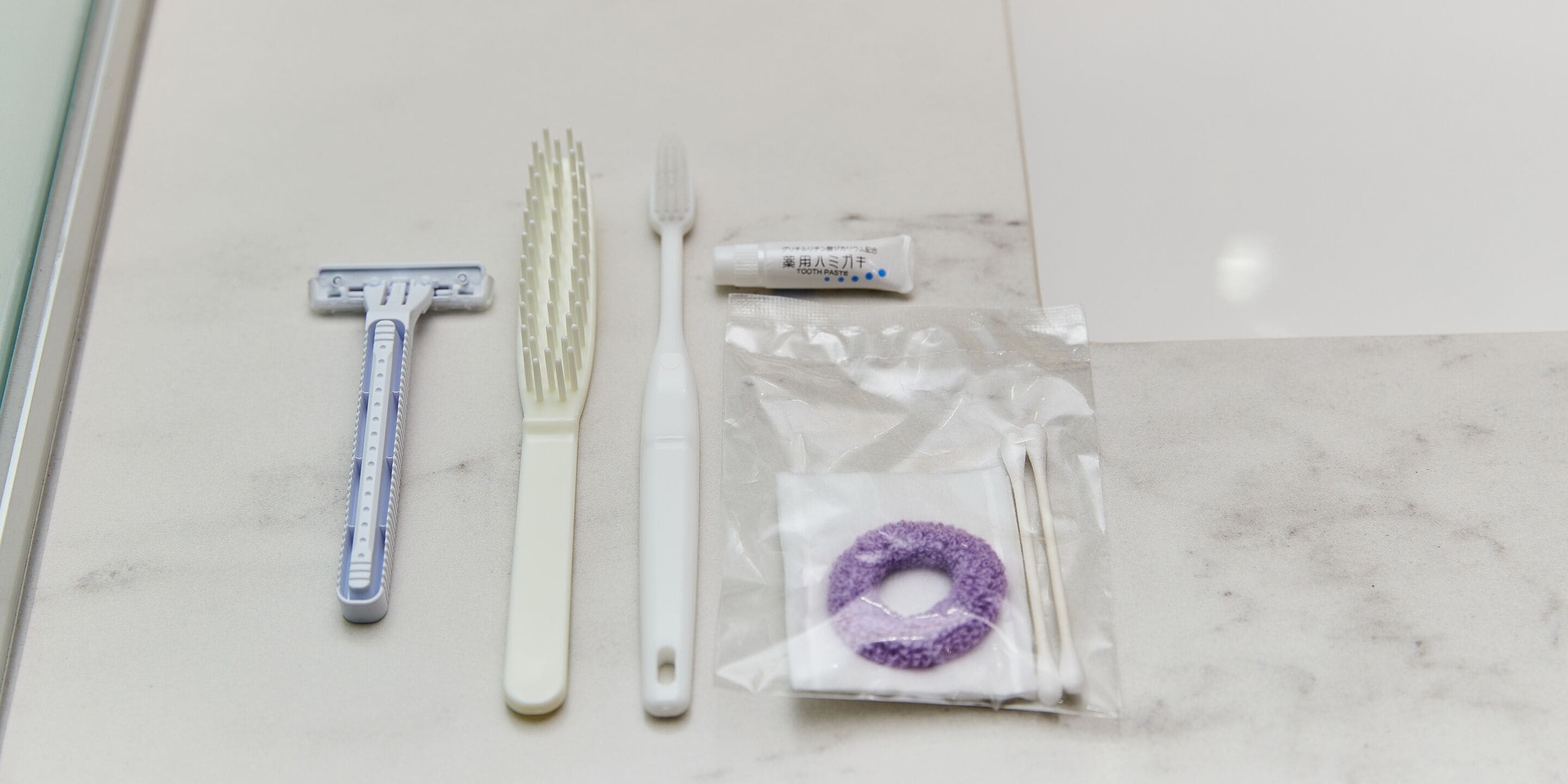 A bathroom with a white countertop, a razor, a toothbrush, and a tube of toothpaste.