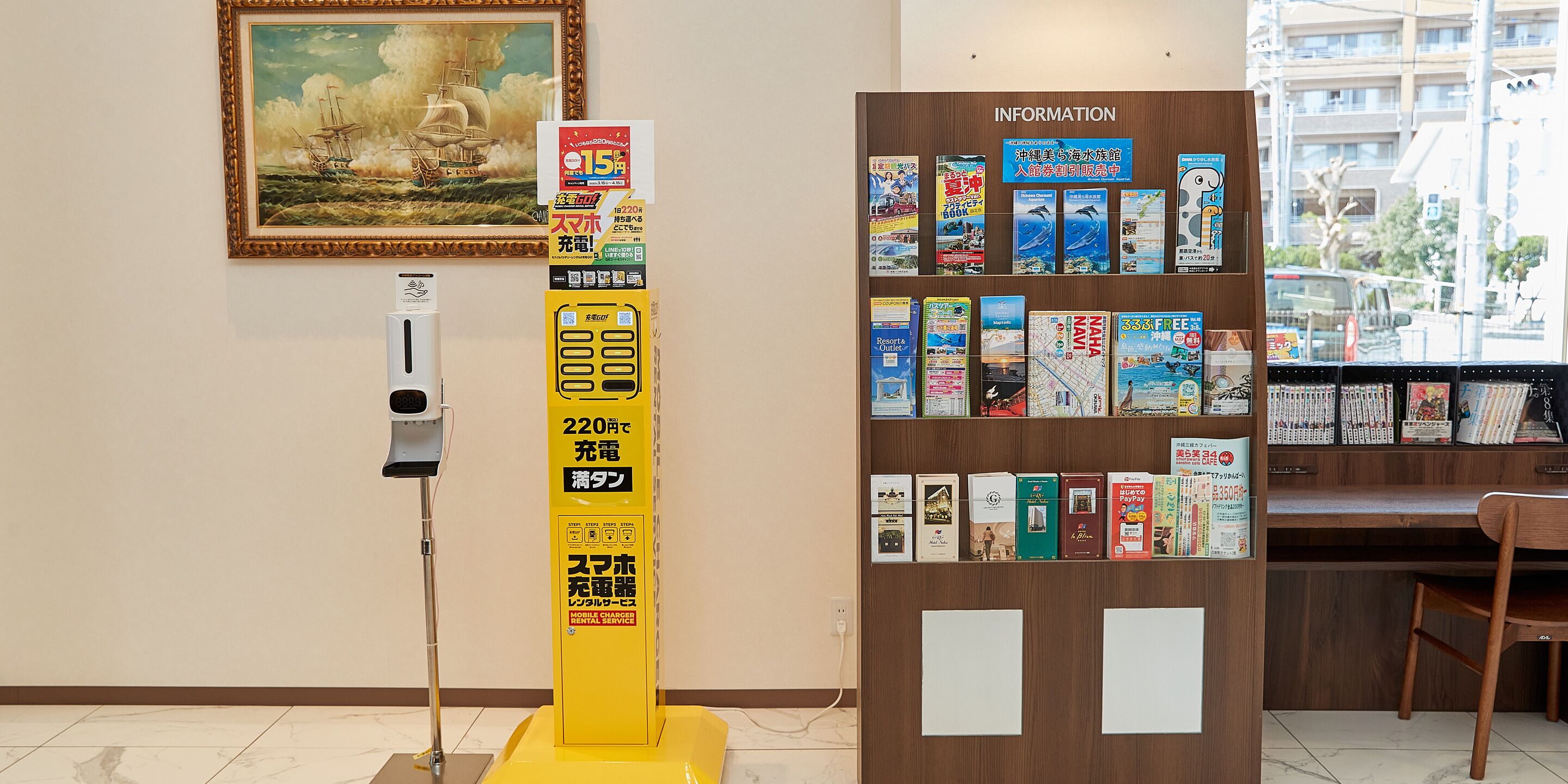 Un espacio público con una estación de carga móvil amarilla, un panel informativo fijado a la pared y una colección de libros y revistas.