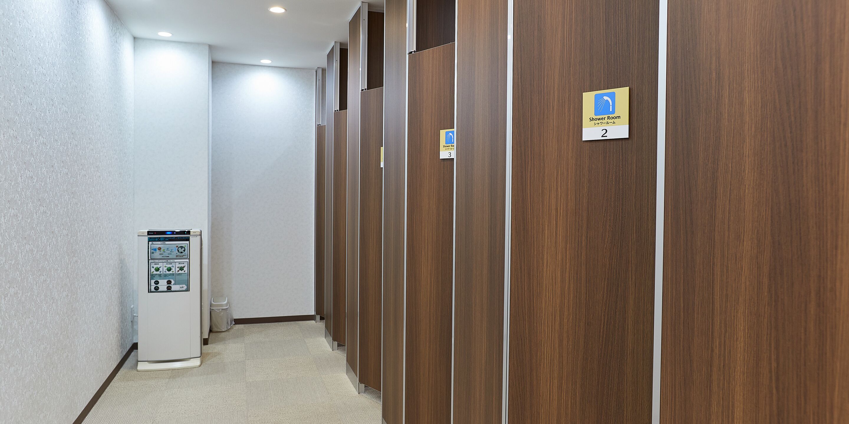 A hallway with wooden partitions, a water dispenser, and signs indicating a shower room.