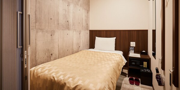 A hotel room with a bed, a wooden headboard, a nightstand with a lamp, and a shoe rack. - Grand Cabin Hotel Naha Oroku (Naha)