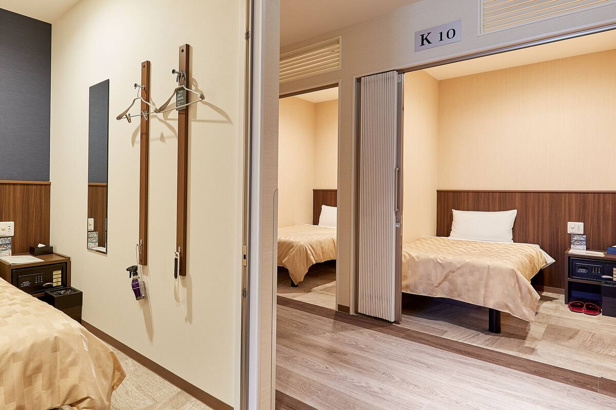 A hotel room with two beds, a wooden headboard, a bedside table with a lamp, and a mirror.