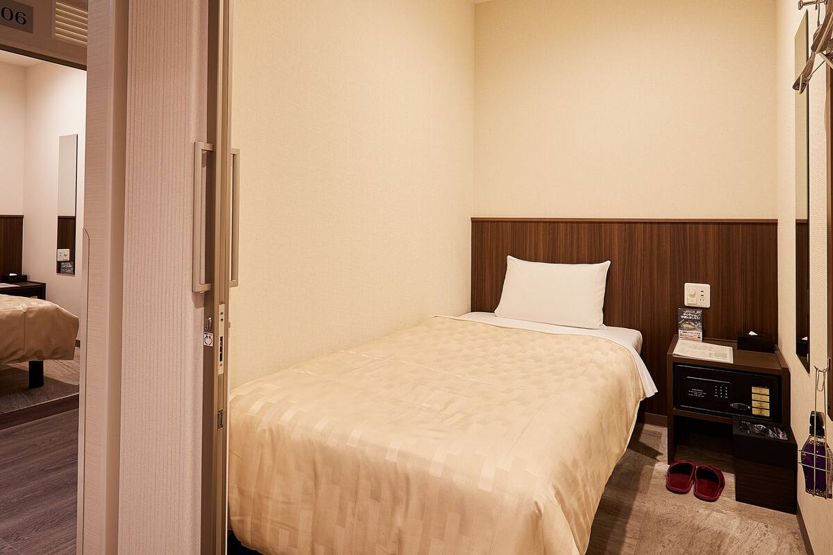 A hotel room with a bed, a nightstand, a mirror, and a shoe rack.