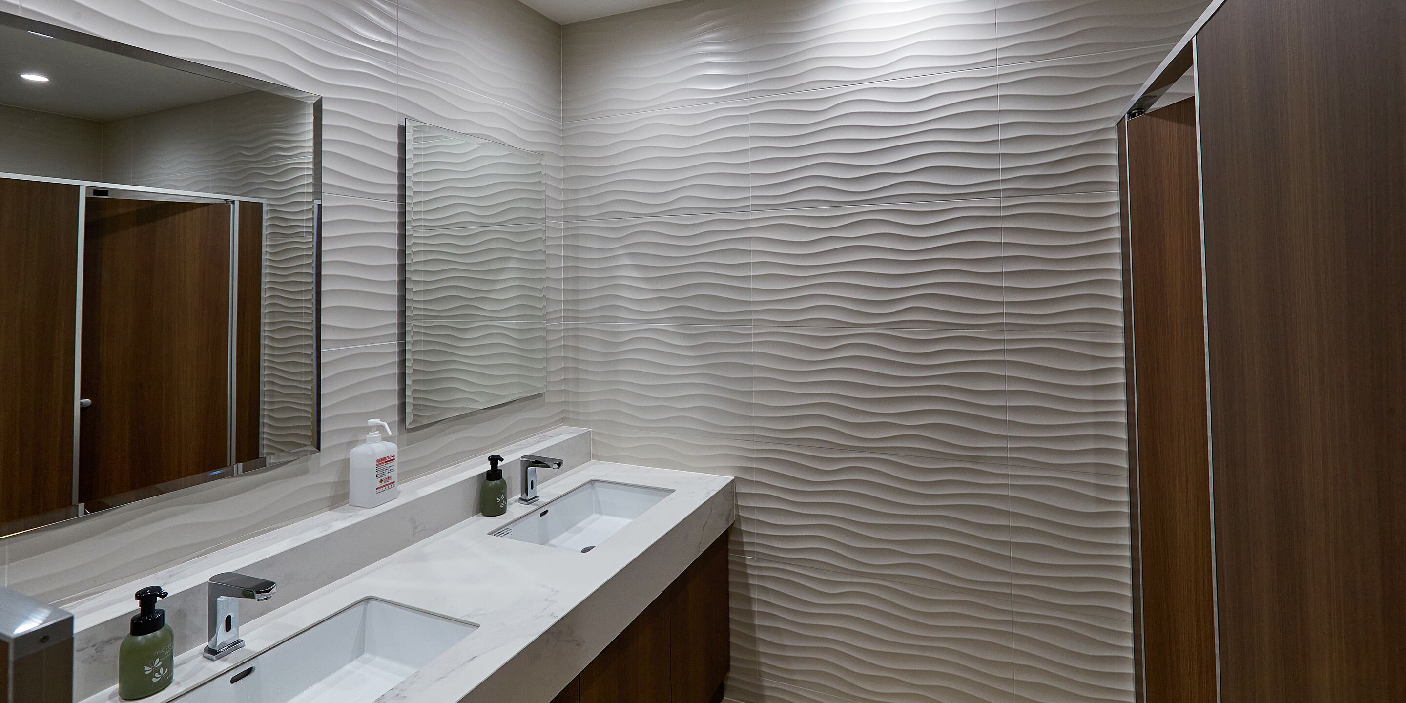 Un baño moderno con dos lavamanos, un espejo grande y una pared con textura.