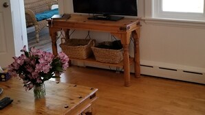 A living room with a wooden coffee table, a black leather couch, a flat-screen TV on a wooden stand, a ceiling fan, and a window with blinds. - Beachside Family Getaway! 3 Doors From Beach Access. Fantastic!!!! (Biddeford)
